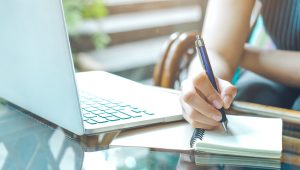 Business woman hand is writing on a notepad with a pen and using a laptop computer. Business woman hand is writing on a notepad with a pen and using a laptop computer.Web banner.